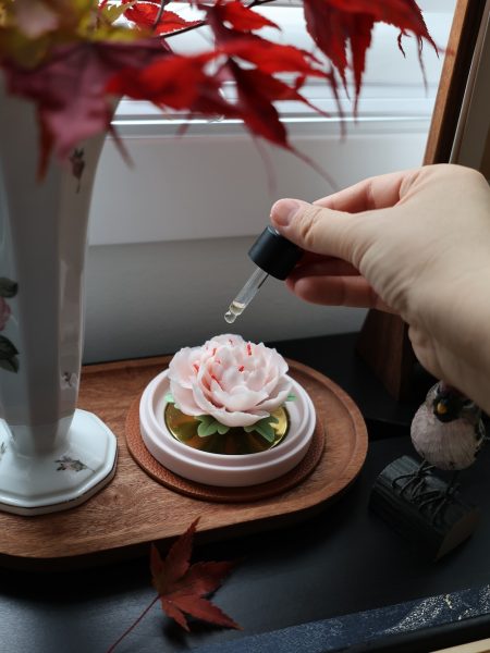 Applying essential oil to a hand-pinched pink porcelain flower diffuser in a warm, artistic home setting.