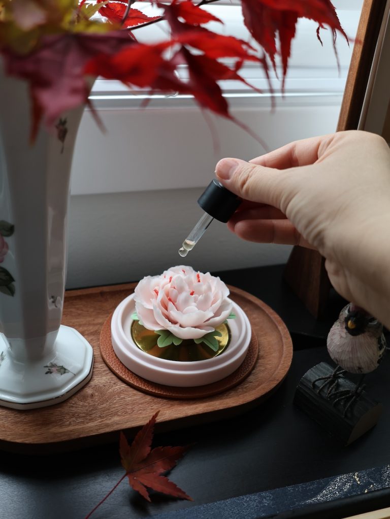 Applying essential oil to a hand-pinched pink porcelain flower diffuser in a warm, artistic home setting.
