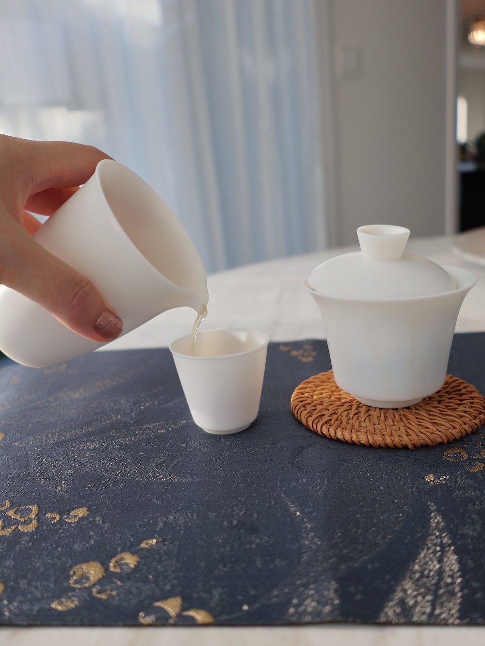 A close-up of a white porcelain tea pitcher pouring tea into a cup, symbolizing the peaceful daily rituals and lifestyle of Home Is Home.